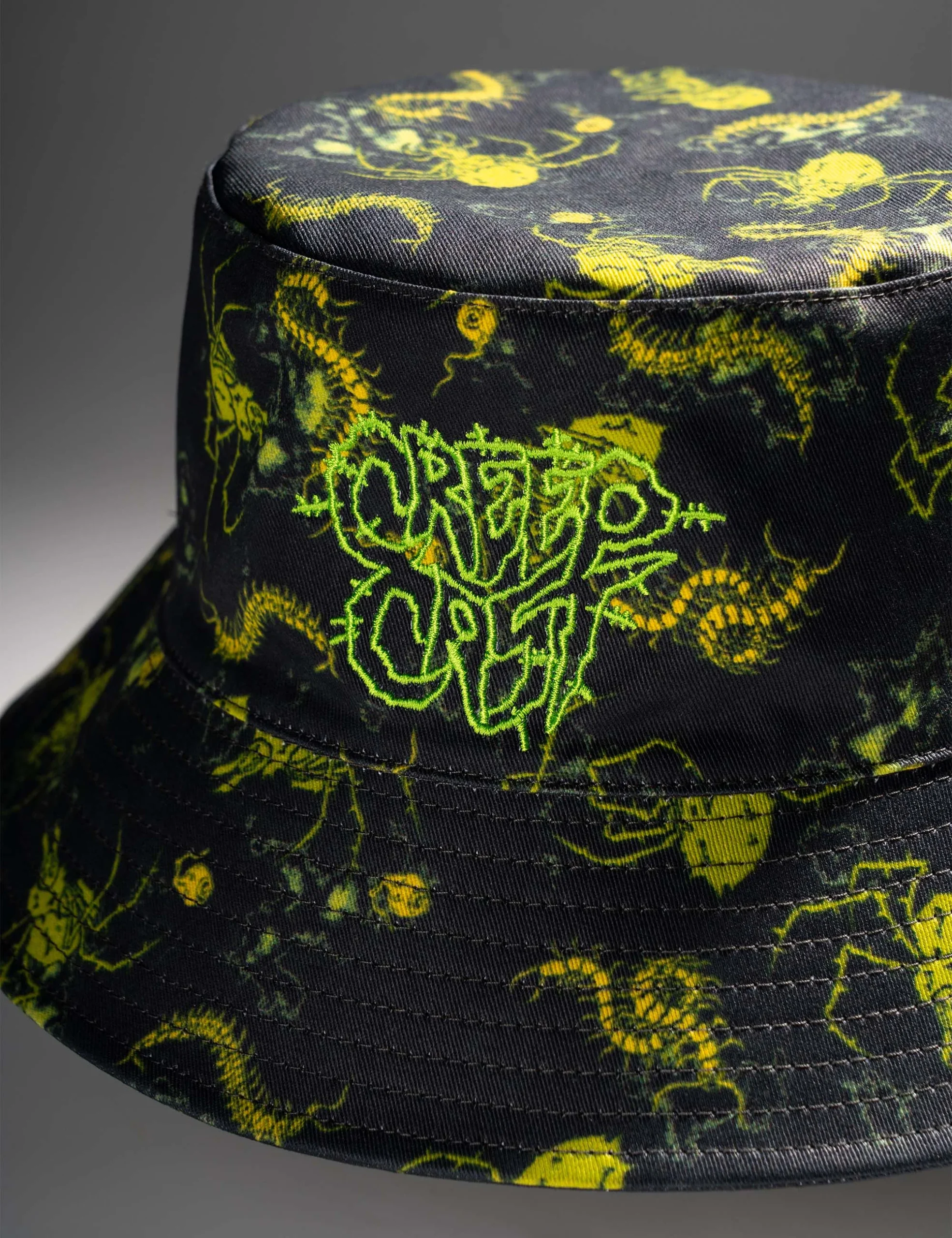 Angled laydown showcasing garment drape and sleeve finishing on the Creepy Crawlies Green Bucket Hat - Creep Cast Merch